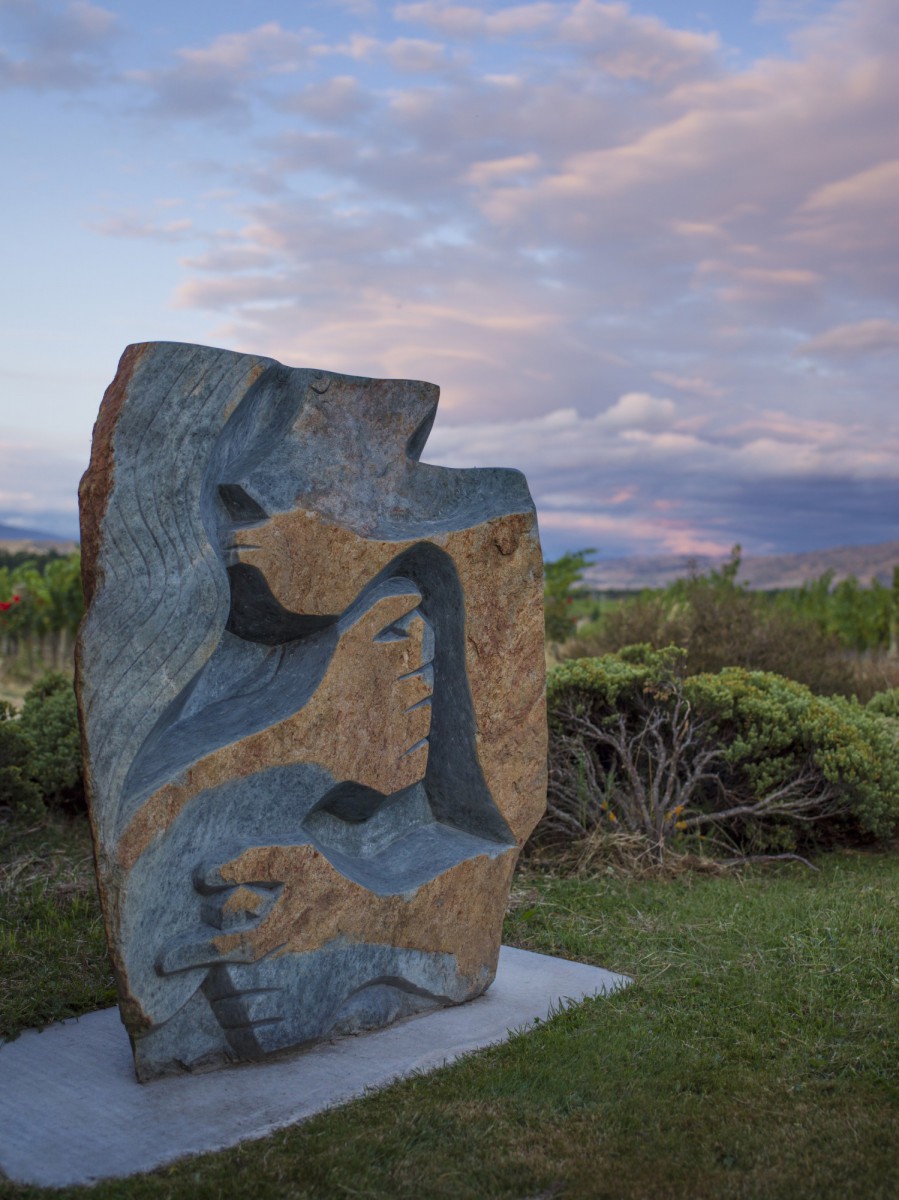 A carved stone sculpture on the lawn at dusk, the vineyard and ranges behind